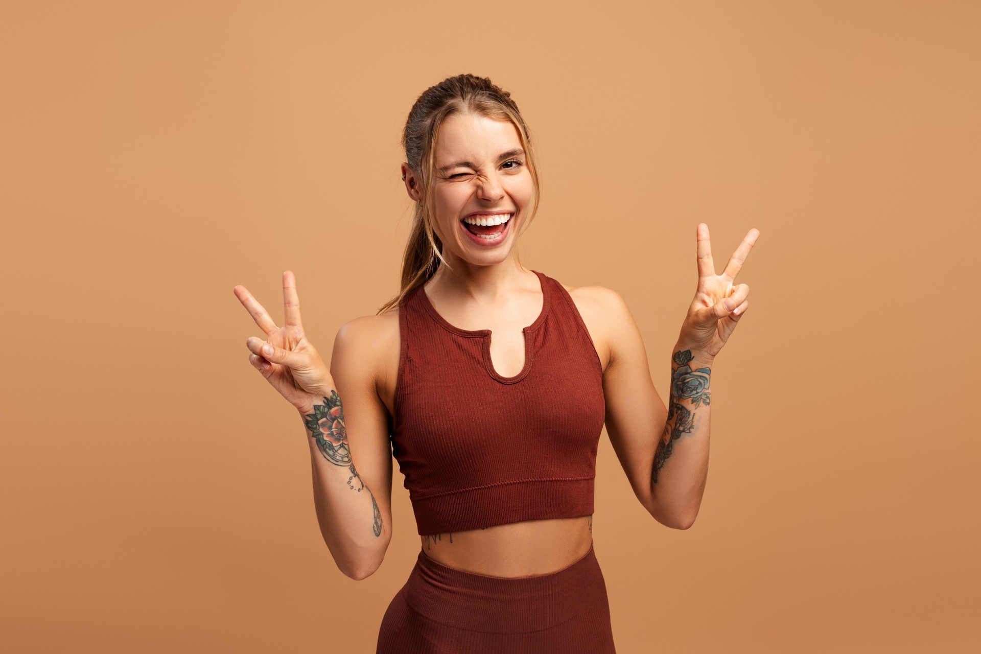 Happy young fit woman winking showing victory sign, looking at camera in studio